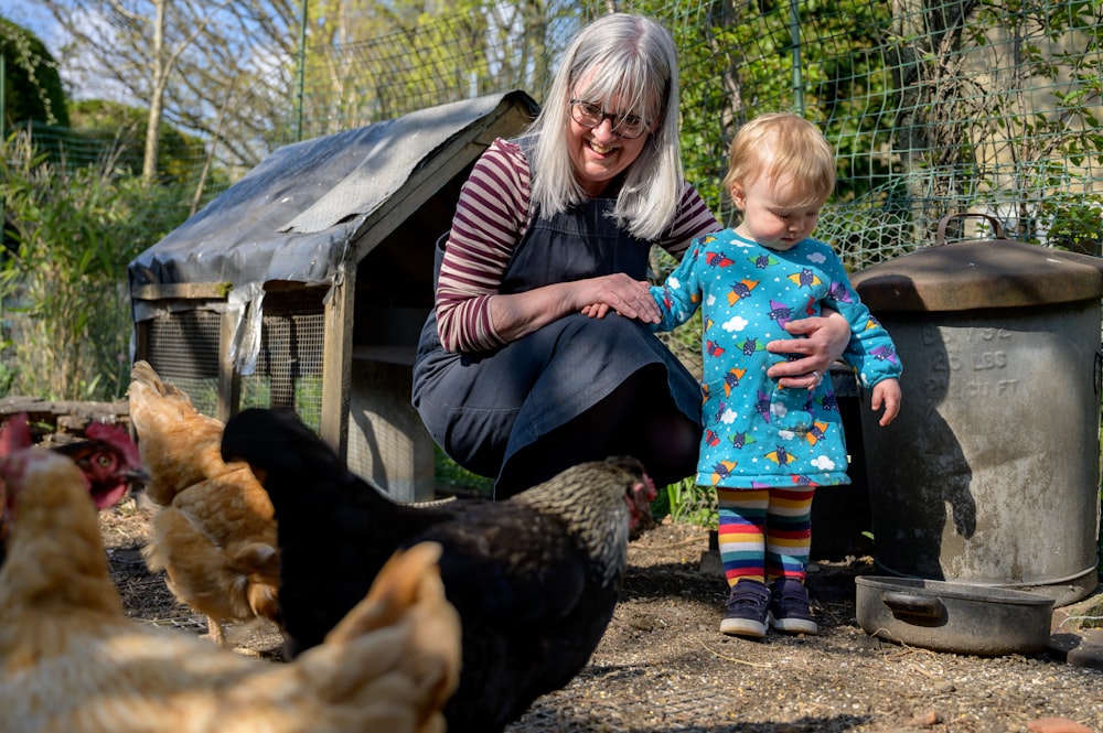 a woman holding a baby next to chickens